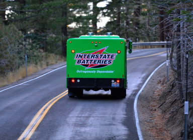 Back of a Green Interstate Battery delivery truck driving along forest road.