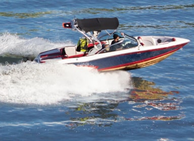 Man in black beanie and black shirt driving a navy blue, red, and white speed boat.